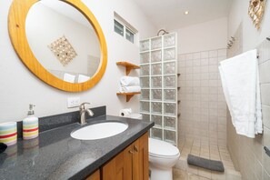 Kylpyhuoneessa on pyöreä peili, pesuallas, wc ja lasinen suihkuseinä.