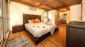 A bedroom with a large bed, wooden flooring, a nightstand, and a dresser.