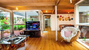A modern interior with a wooden ceiling, a TV on a wooden stand, a wicker chair, and a glass table with a decorative centerpiece.