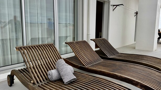 Une pièce moderne avec deux fauteuils en bois, une grande fenêtre avec des rideaux et une porte bien visible.