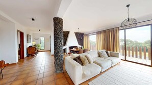 A spacious living room with a stone pillar, a sofa, a dining table, and a view of the outdoors. - Azores Quinta DA Cruzinha (Lagoa)