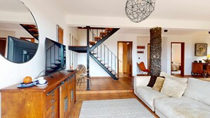 A spacious living area with a staircase, a television, a wooden cabinet, and a large pillar. - Azores Quinta DA Cruzinha (Lagoa)