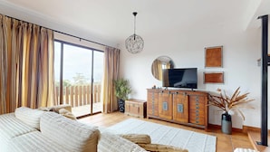 A spacious living room with a large sliding glass door, a wooden cabinet with drawers, a flat-screen TV, and a hanging spherical light fixture. - Azores Quinta DA Cruzinha (Lagoa)