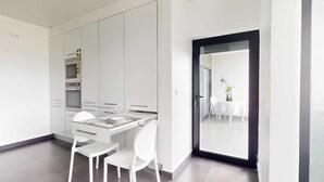 Eine moderne Küche mit weißen Schränken, einem Esstisch für zwei Personen und einer schwarzen Tür, die auf einen Balkon mit Blick führt.