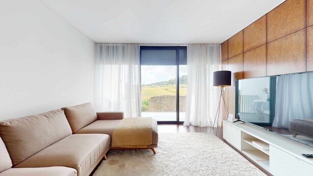 Ein modernes Wohnzimmer mit einer Couch, einem Flachbildfernseher und Blick auf ein Feld durch ein großes Fenster.