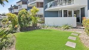 A modern multi-story residential building with balconies, a well-maintained lawn, and a variety of plants.