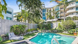A swimming pool with a wooden deck, a hot tub, and a lounge chair.