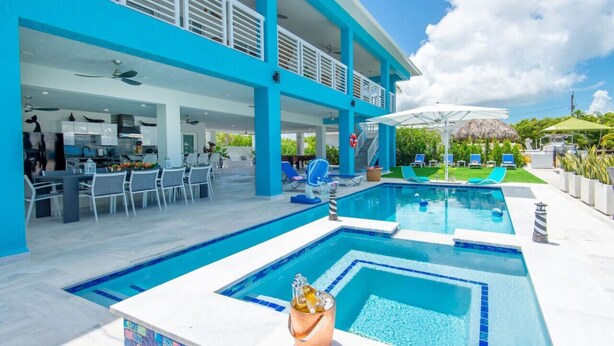 A modern pool area with a bar and outdoor seating, surrounded by a blue building with a covered patio.