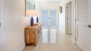 A hallway with a wooden console table, two lamps, a mirror, and a double door with a glass panel.