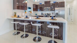 A modern kitchen with a central island, bar stools, stainless steel appliances, and pendant lighting.
