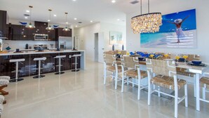 A modern kitchen with a central island, bar stools, and a dining area with white chairs.