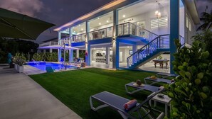 A modern two-story house with a swimming pool, outdoor seating, and a well-lit balcony.