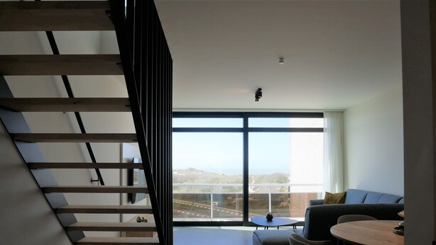 A modern living room with a staircase, a sofa, a dining table, and a view of the outdoors.