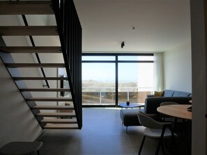 Una sala moderna con una escalera, un sofá, una mesa de comedor y vistas al exterior.