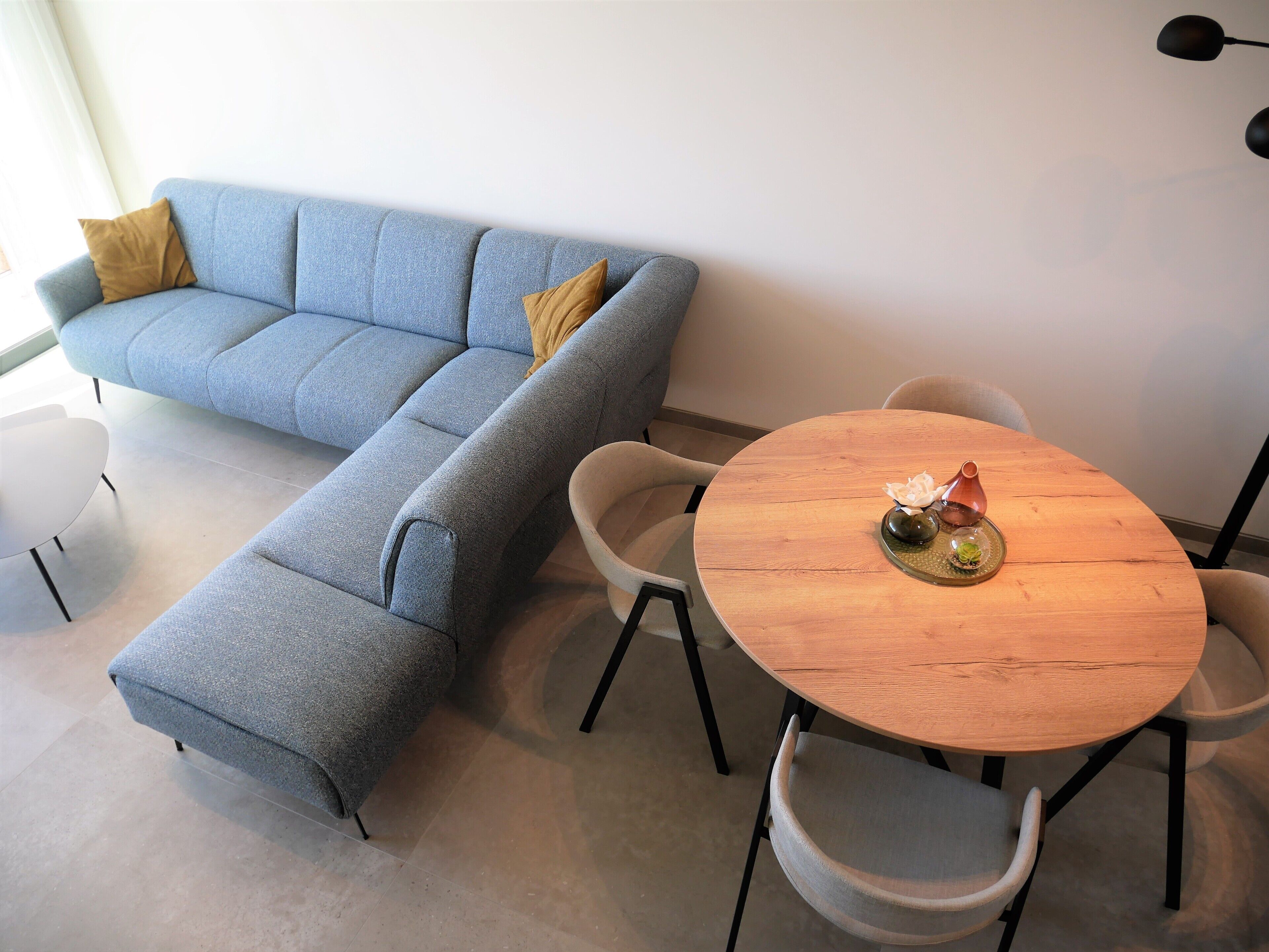 A modern living room with a grey sectional sofa, a round wooden coffee table, and two white chairs.