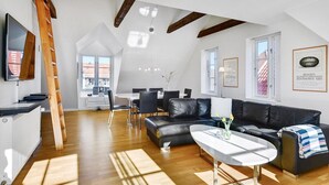 Una sala de estar moderna con un sofá de cuero negro, una mesa de centro blanca y un comedor con una mesa y sillas blancas.