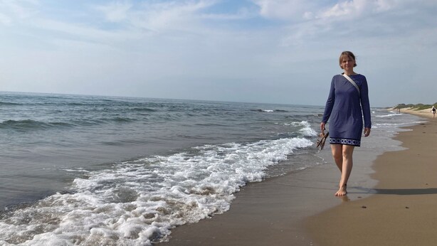 Una playa con olas, una persona caminando y un cielo despejado.