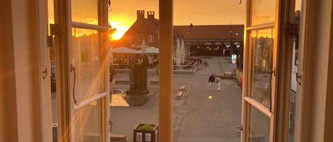 An open window with a view of a street at sunset, including buildings and a statue.