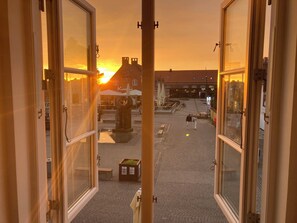Auki oleva ikkuna, josta avautuu näkymä kadulle auringonlaskun aikaan. Näkymään kuuluu rakennuksia ja patsas.
