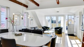 Una sala de estar moderna con una mesa de comedor, sofás negros y una araña.