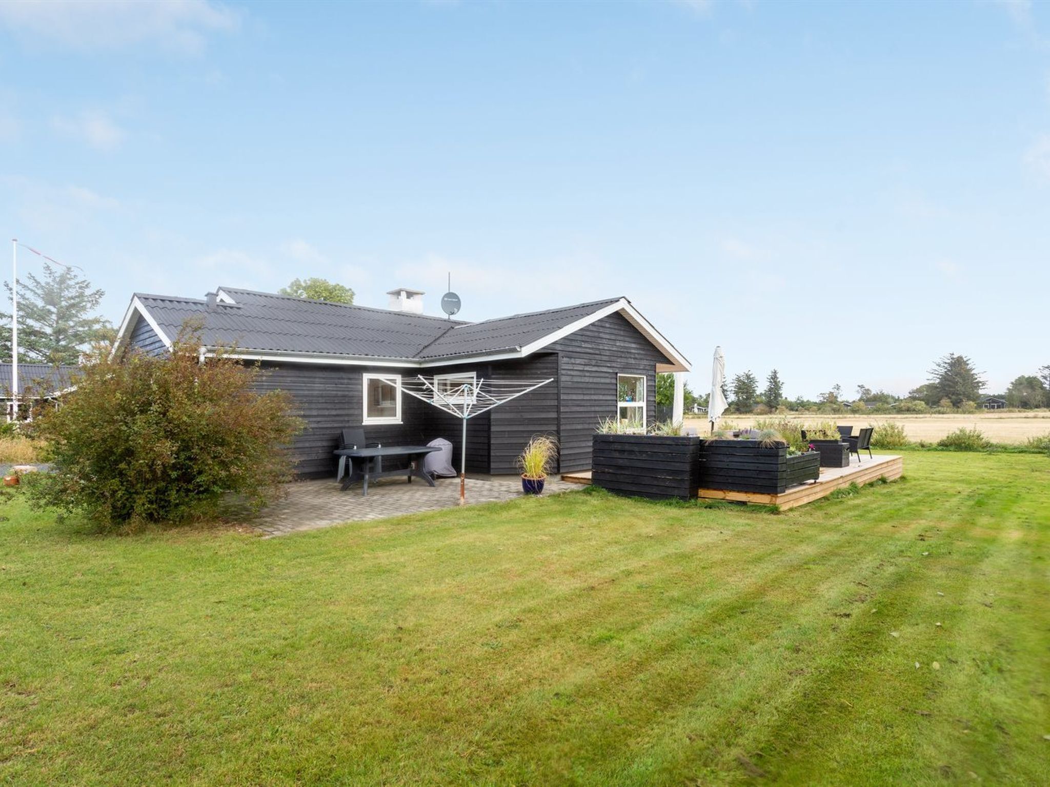 A single-story house with a dark exterior, a satellite dish, a patio with outdoor furniture, and a well-maintained lawn.