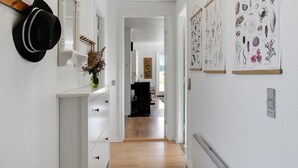 Ein Flur mit weißen Wänden, Holzboden und einem schwarzen Hut, der links hängt. An der rechten Wand befinden sich gerahmte botanische Illustrationen.
