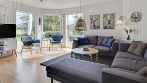 Ein modernes Wohnzimmer mit einem grauen Sofa, blauen Sesseln, einem Fernseher und Kunstwerken an den Wänden.