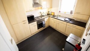 A compact kitchen with light wooden cabinets, a black countertop, a stove, and a window with a view. - Tranquil 2Bed/2Bath Duplex Falkirk (Falkirk)