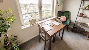A room with a dining table and chairs, a green chair, a window with a view of buildings, and a shelf with decorative items. - Tranquil 2Bed/2Bath Duplex Falkirk (Falkirk)