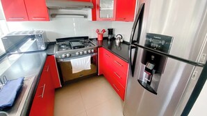 Uma cozinha compacta com armários vermelhos, um fogão de aço inoxidável e uma geladeira.
