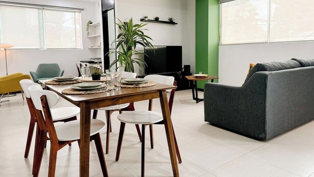 Uma sala de estar moderna com área de jantar, um sofá cinza e uma TV.