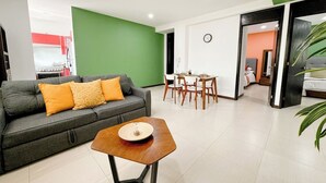Uma sala de estar moderna com um sofá cinza, uma mesa de centro de madeira e um espaço de refeições com cadeiras e mesa de madeira.