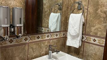 A bathroom with a white sink, marble tiles, a mirror, and two hand soap dispensers.