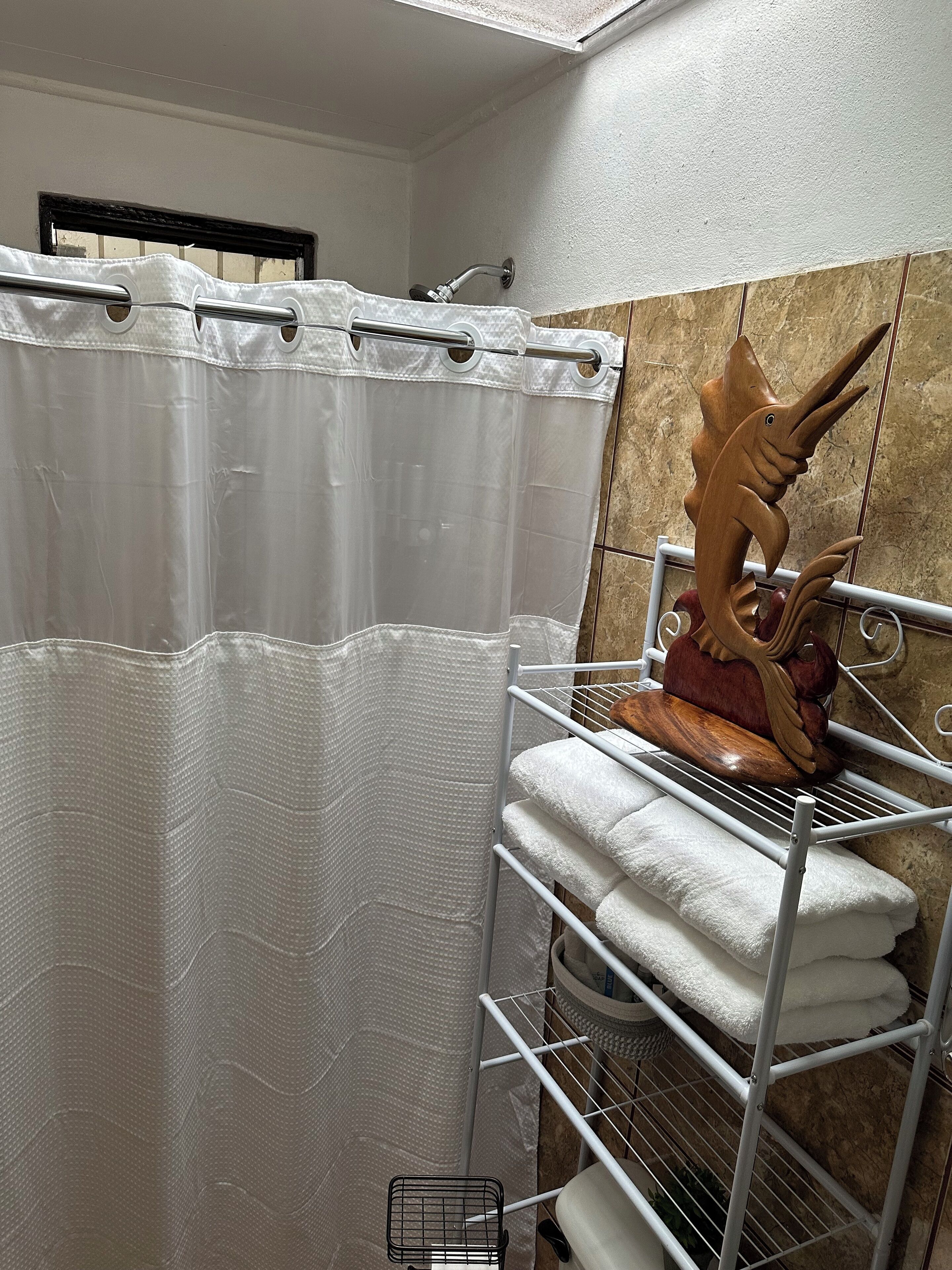 Une salle de bain avec un rideau de douche, un porte-serviettes avec des serviettes pliées et une sculpture décorative en bois représentant un poisson.