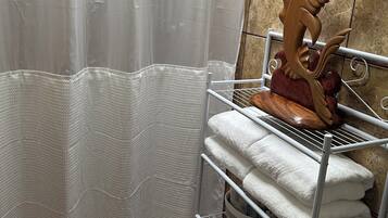 Une salle de bain avec un rideau de douche, un porte-serviettes avec des serviettes pliées et une sculpture décorative en bois représentant un poisson.