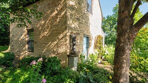 A stone building with a window and a door, surrounded by greenery and flowers.