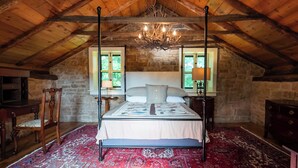 A bedroom with a four-poster bed, stone walls, wooden beams, and a chandelier.