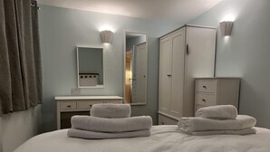 A neatly made bed with folded towels, a mirror, a wardrobe, and a light switch on the wall. - Charming Woodland Lodge 2 person 1 bedroom (Great Yarmouth)