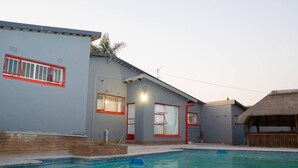 Un espace piscine avec une maison, une structure à toit de chaume et un ciel dégagé.