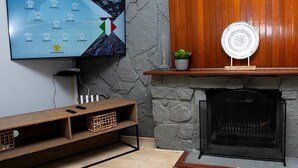 Un salon avec un téléviseur diffusant un match de football, une cheminée et un mur en pierre.
