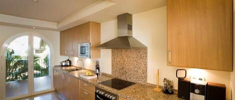 A modern kitchen with granite countertops, wooden cabinets, a stainless steel range hood, and a built-in microwave.