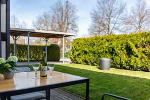 Une terrasse extérieure avec une table, deux verres à vin, une bouteille de vin et une plante en pot.