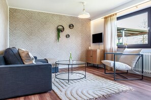 Un salon moderne comprenant un canapé, une table basse ronde, un fauteuil, un téléviseur et une fenêtre avec des rideaux.