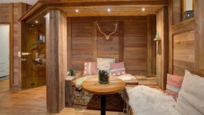 Interior acogedor de una cabaña de madera con chimenea, un banco con almohadones y una mesa de vidrio con un objeto decorativo.
