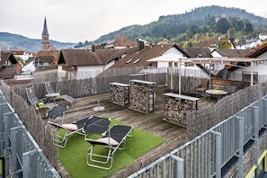 A rooftop terrace with lounge chairs, a table, and a view of a church and hills.