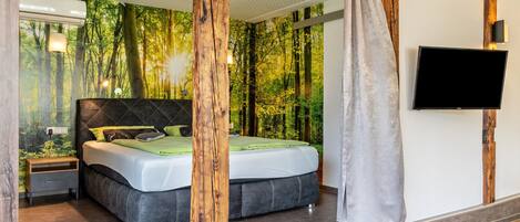 A modern bedroom with a large bed, a TV, and a forest-themed wall mural.