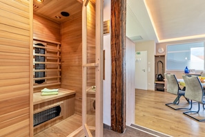 A sauna room with wooden walls and a glass door, a wooden bench, and a towel.