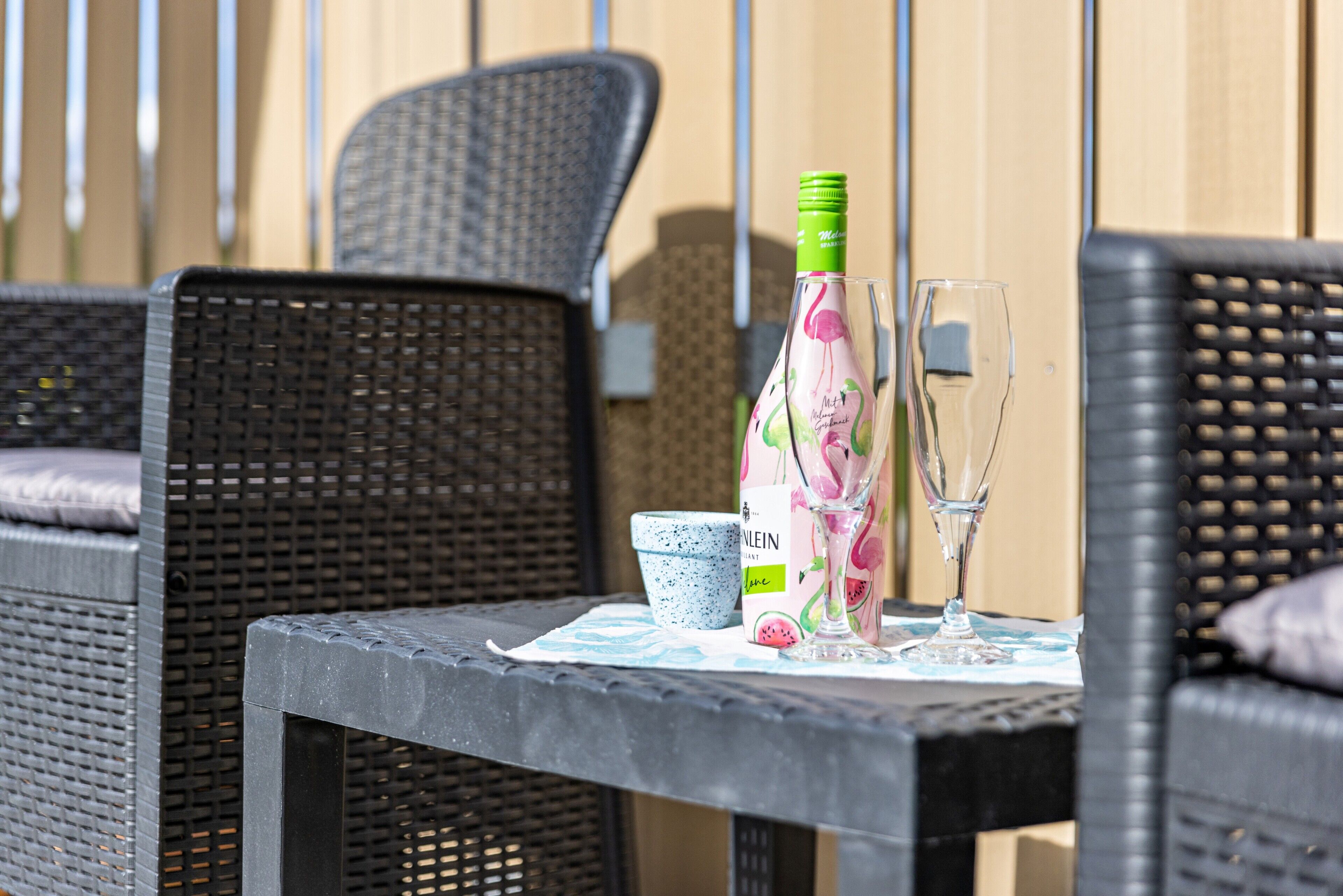 Une chaise en osier, une table avec une bouteille et un verre, et une petite tasse bleue et blanche.