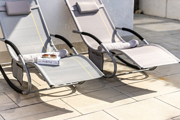 Two sun loungers with towels and sunglasses on them, placed on a tiled patio.