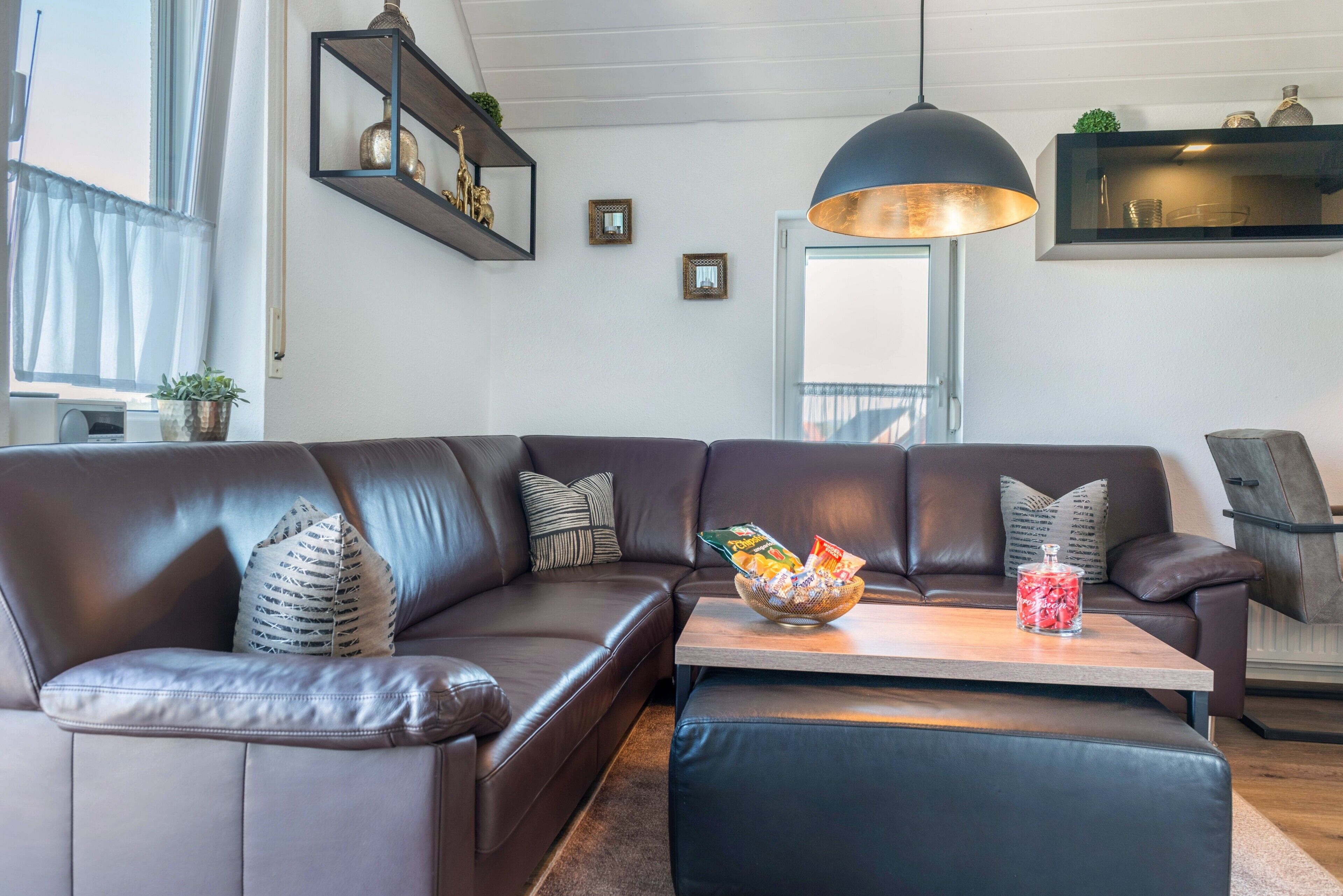 Een moderne woonkamer met een leren hoekbank, een houten salontafel en een grote hanglamp.